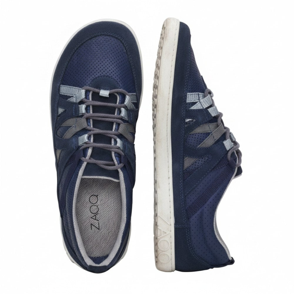 Wir präsentieren den DRAQE Azul von ZAQQ: Ein Paar Sportschuhe in Dunkelblau mit weißer Sohle und hellgrauen Schnürsenkeln, entworfen für maximalen Tragekomfort. Die Draufsicht des linken Schuhs unterstreicht sein schlankes Design, während das Seitenprofil des rechten Schuhs ein markantes ZAQQ-Logo auf der Sohle aufweist.