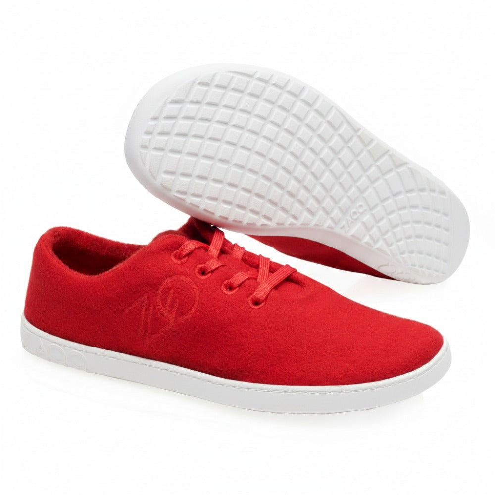 Die LIQE Race Sneaker von ZAQQ werden kunstvoll vor einem weißen Hintergrund präsentiert. Ein Sneaker liegt auf der Seite und zeigt die strukturierte graue Sohle, während der andere aufrecht steht. Rote Schnürsenkel ergänzen das Obermaterial aus Stoff und schaffen einen lebendigen und dennoch entspannten Stil.