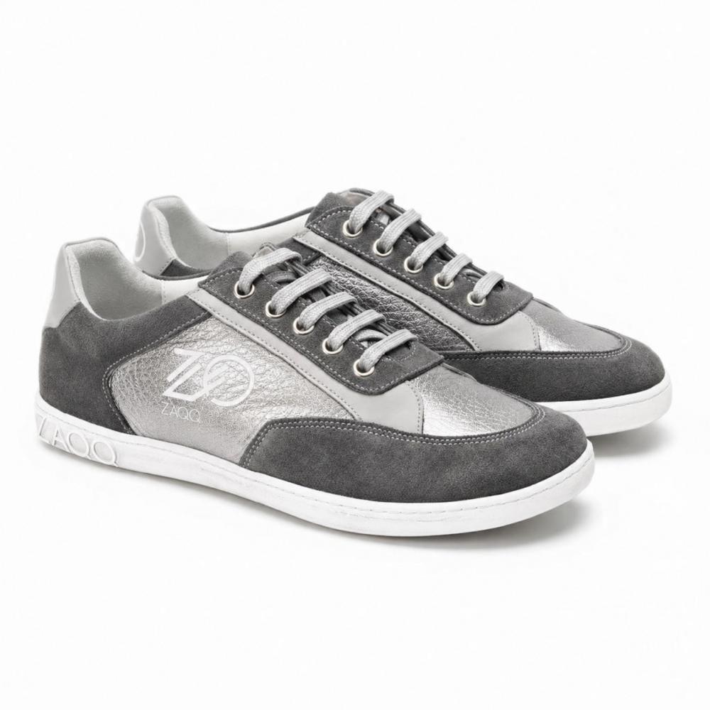 Pár OQTAV Grey tenisek od ZAQQ, vyrobených z jemné semiše a strukturovaných vložek. Se stříbrnými tkaničkami a charakteristickým logem Zagoo na boku a patě jsou tyto stylové boty prezentovány vedle sebe na bílém pozadí.