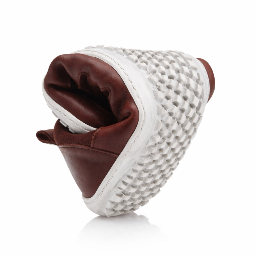 Der SHOQQ Dark Brown von ZAQQ ist ein einzigartiger Sneaker mit einem Obermaterial aus braunem Leder, das fachmännisch gefaltet wurde, um seine beeindruckende Flexibilität zu zeigen. Seine Sohle weist ein auffälliges schwarz-weißes Karomuster auf, das das unverwechselbare Design des Schuhs unterstreicht.