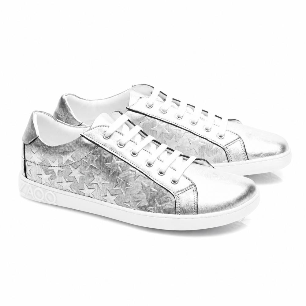 Tenisky SLOQ Stars Silver od ZAQQ mají bílé tkaničky a hvězdicový vzor na bocích, doplněné bílou podrážkou s nápisem VAOO na patě. Tyto boty se vyznačují elegantním a moderním designem s lesklým metalickým povrchem.