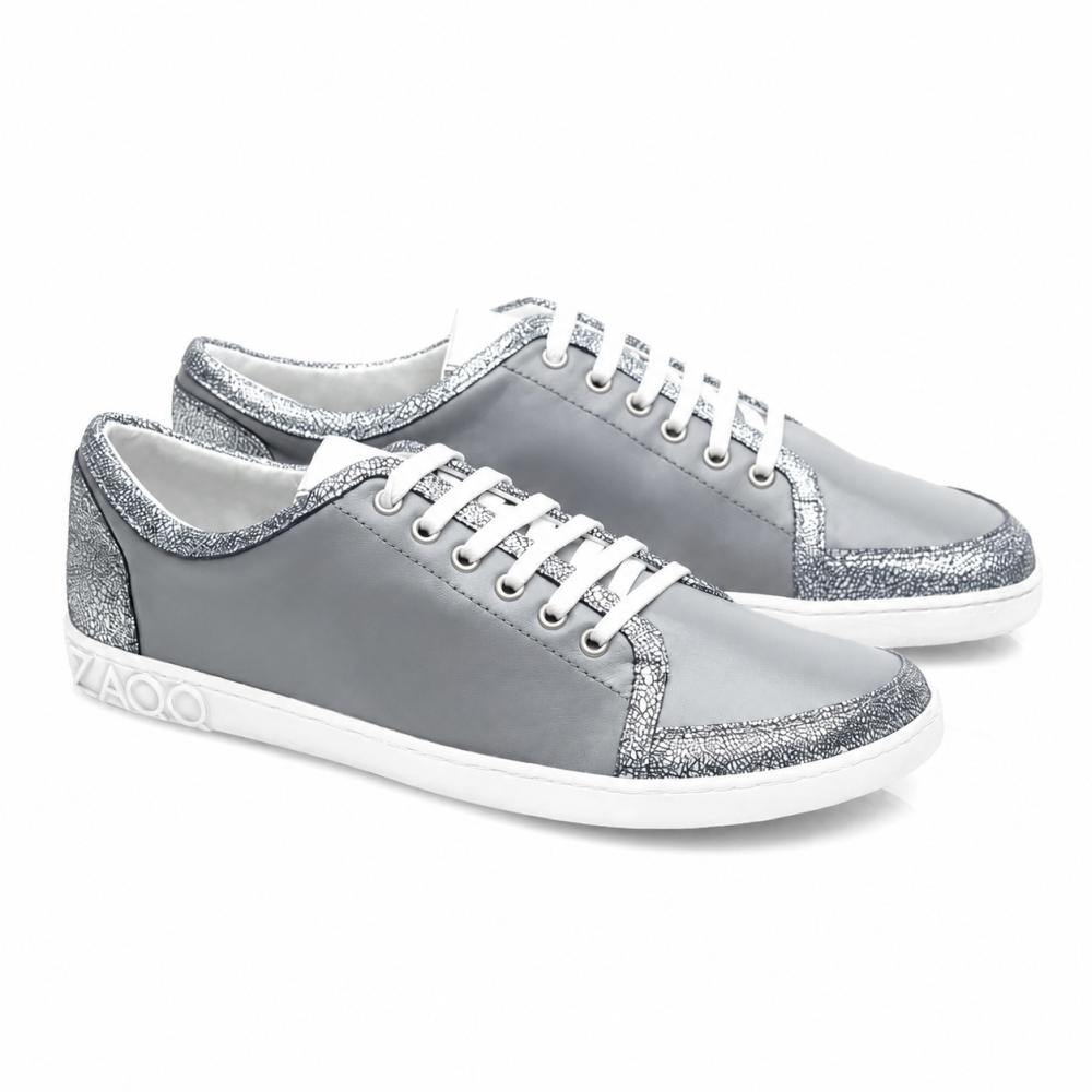 Tenisky TIQQ Grey Silver od ZAQQ zaujmou svým jednoduchým designem z měkké nappa kůže s bílými tkaničkami a stříbrnými třpytivými akcenty, doplněné bílými podrážkami a decentním logem na patě, a nabízejí dokonalou kombinaci stylu a pohodlí pro každou příležitost.